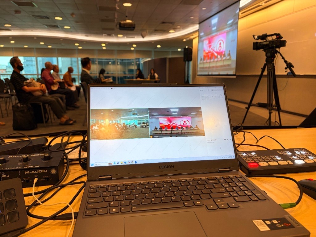 Production desk at a hybrid AGM: VooV Meeting showing the Singapore room and the China room, with shareholders seated and the China feed on the projector.